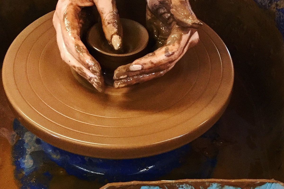 hands on a clay pot on a potter's wheel