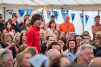 A person giving a presentation in a marquee full with a seated audience 