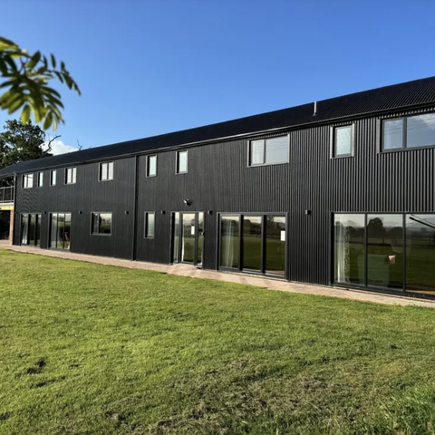 black barn conversion against blue sky with green grass below