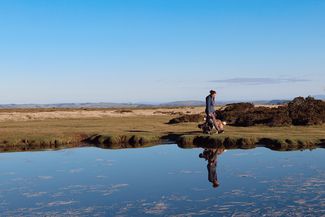 Young woman walking dog reflected in pond on high up landscape