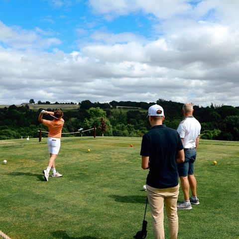 three people standing on golf course overlooking hilly countryside