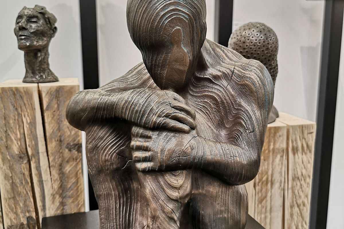 wooden carved sculpture of a person sitting holding their knees to their chest