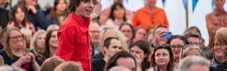 A person giving a presentation in a marquee full with a seated audience 