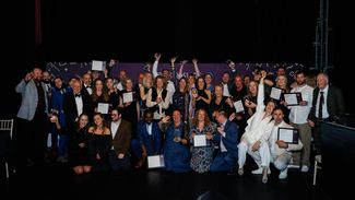 Winners from the Visit Herefordshire Tourism Awards 2025 cheer on stage holding their certificates and trophies.