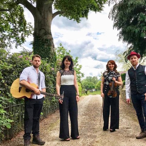 The four members of The Kilpecks standing on a country lane with their musical instruments