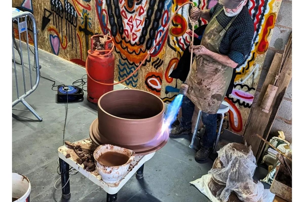 Man with blowtorch and large red clay pot on potter's wheel