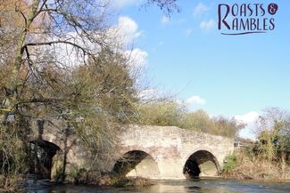 ancient bridge with river flowing through, trees to one side and bright blue skies