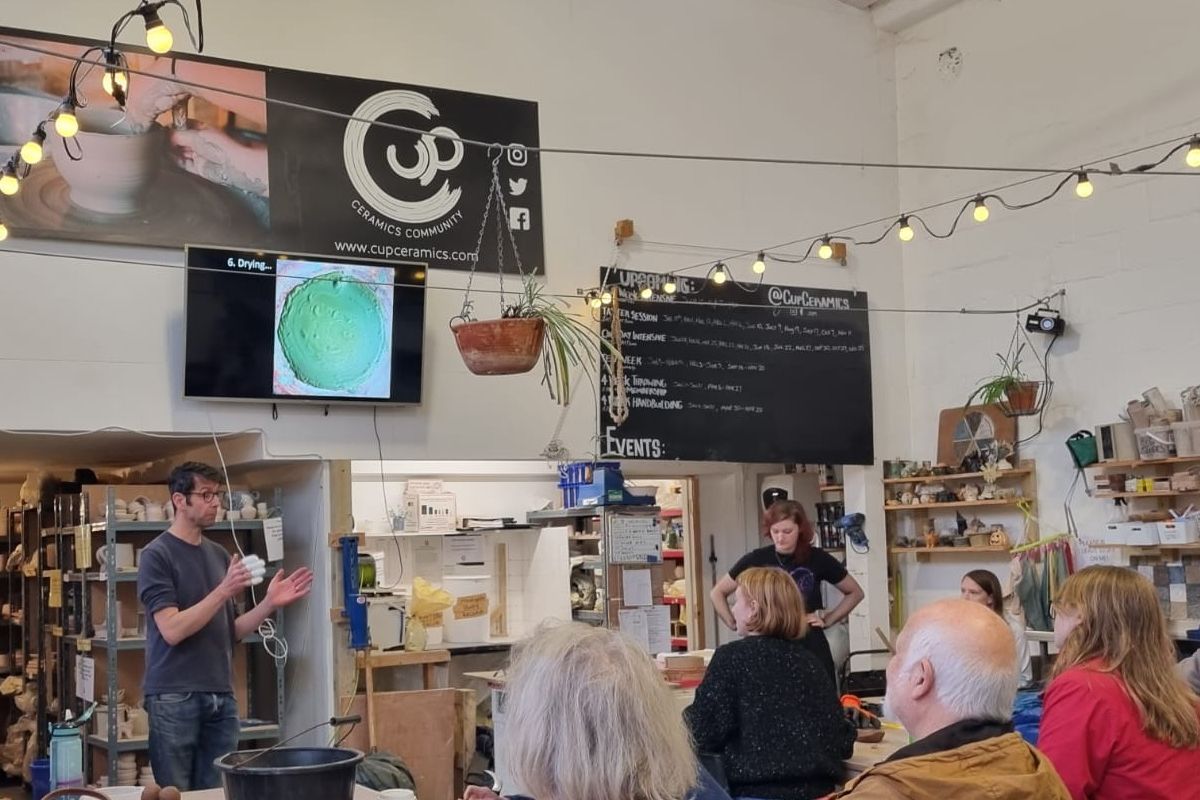 Person giving a talk to a room full of people at pottery workshop