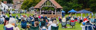An open-air music event with people watching acts on a bandstand in Ross-on-Wye