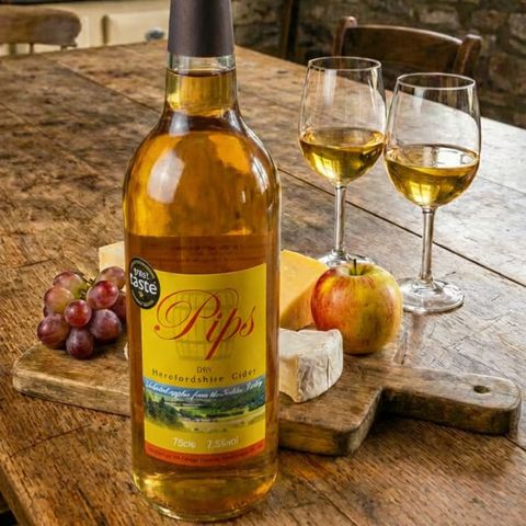 Pips cider on a table with two glasses and a ploughmans platter