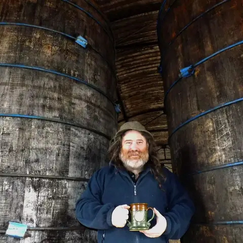 Cider maker stands in front of his barrels