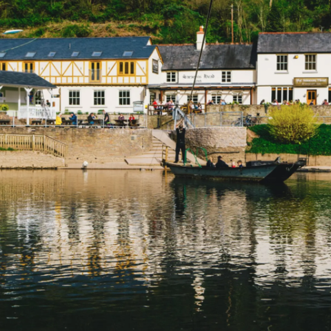 low white buildings on the banks of a river with hand-pull ferry in the foreground